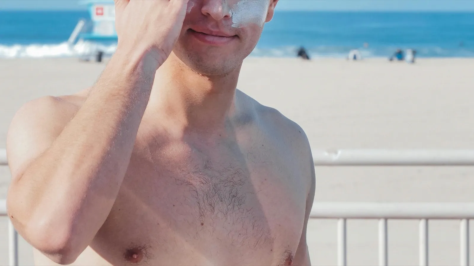 Homem aplicando protetor solar no rosto em ambiente externo de praia