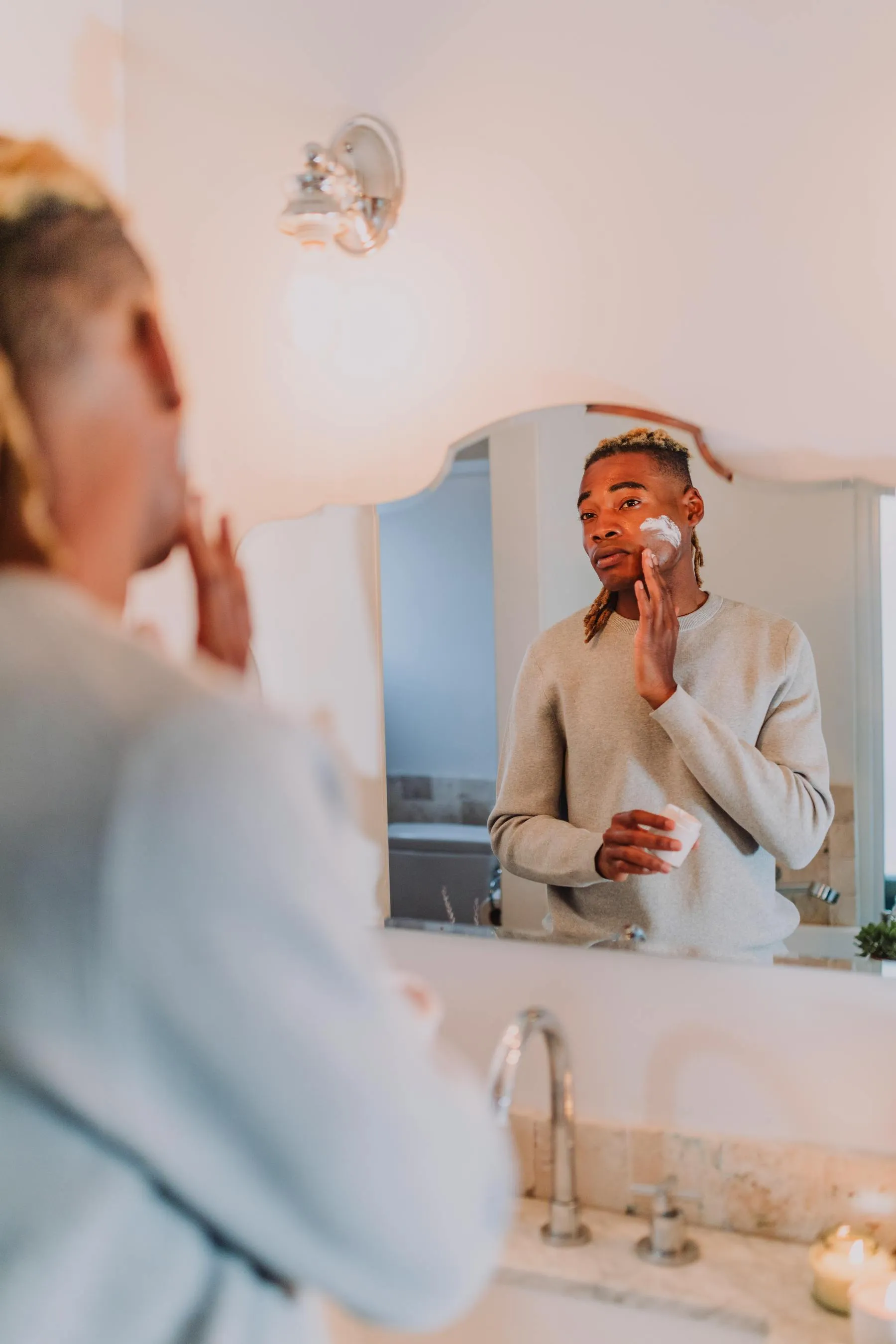 Homem aplicando creme no rosto diante do espelho do banheiro